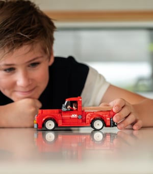 A young boy playing with a red NovaBrix Ace Hardware Vintage Truck